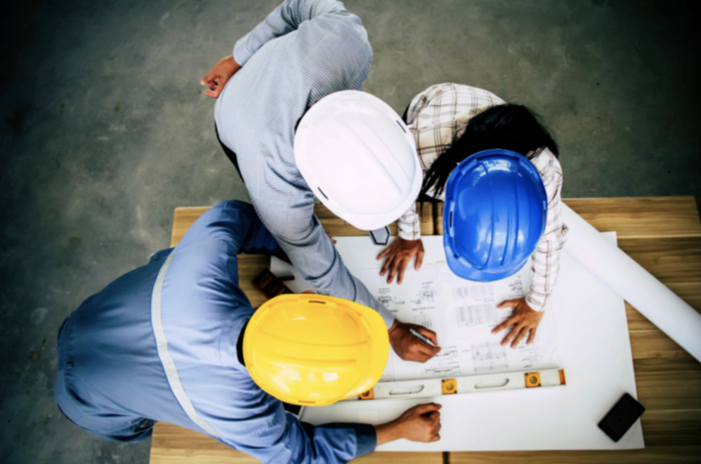 Industrial project management | People in hard-hats gathered around a table with project plans.